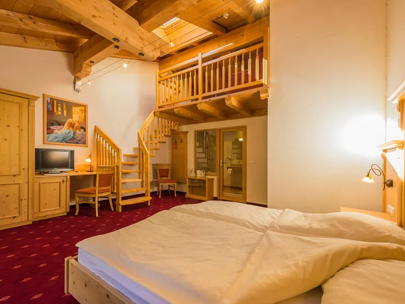 Maisonette-Zimmer der OchsAlm mit Doppelbett, Holzbalkendecke und Treppe zur Galerie-Ebene