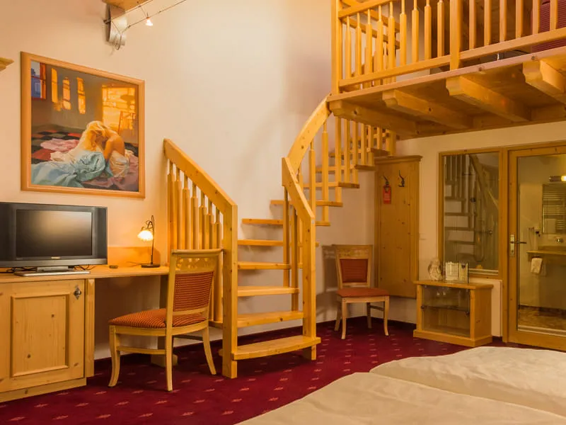 Doppelbett im Holzzimmer der OchsAlm, dahinter Schreibtischplatz und Treppe zur Galerie